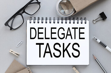 delegate tasks. Gray background. text on notepad near glasses with pen and pencil. business layout.