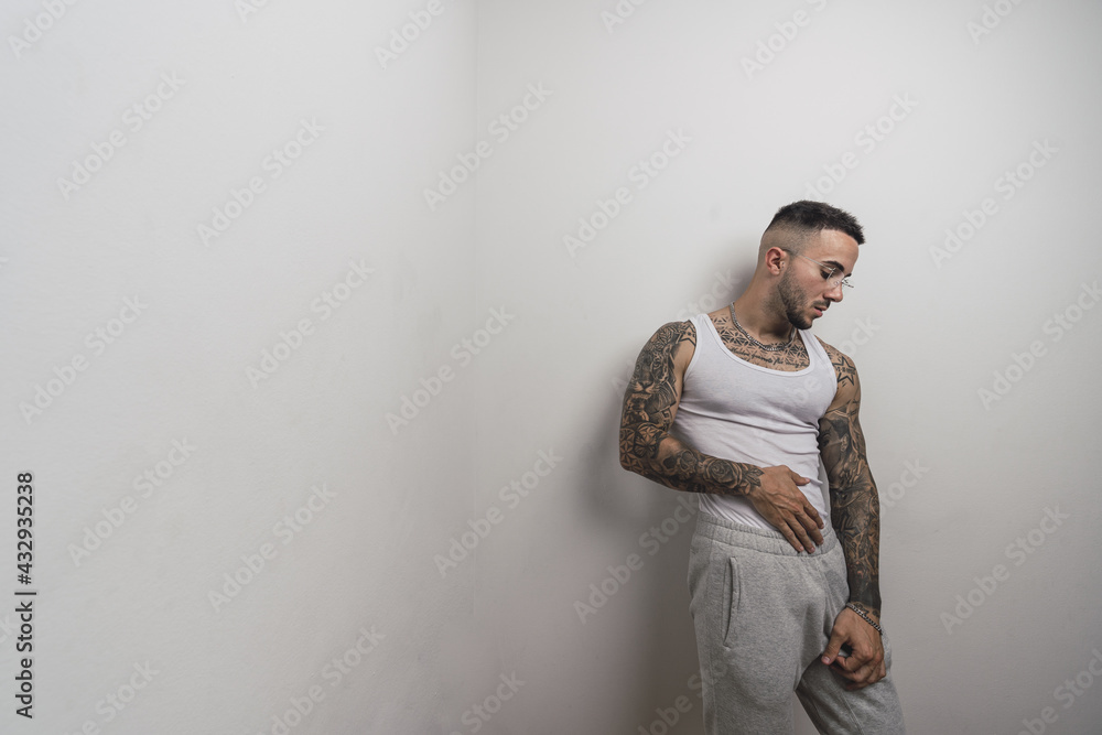 Poster portrait of a young handsome tattooed spanish male posing leaning on a white wall