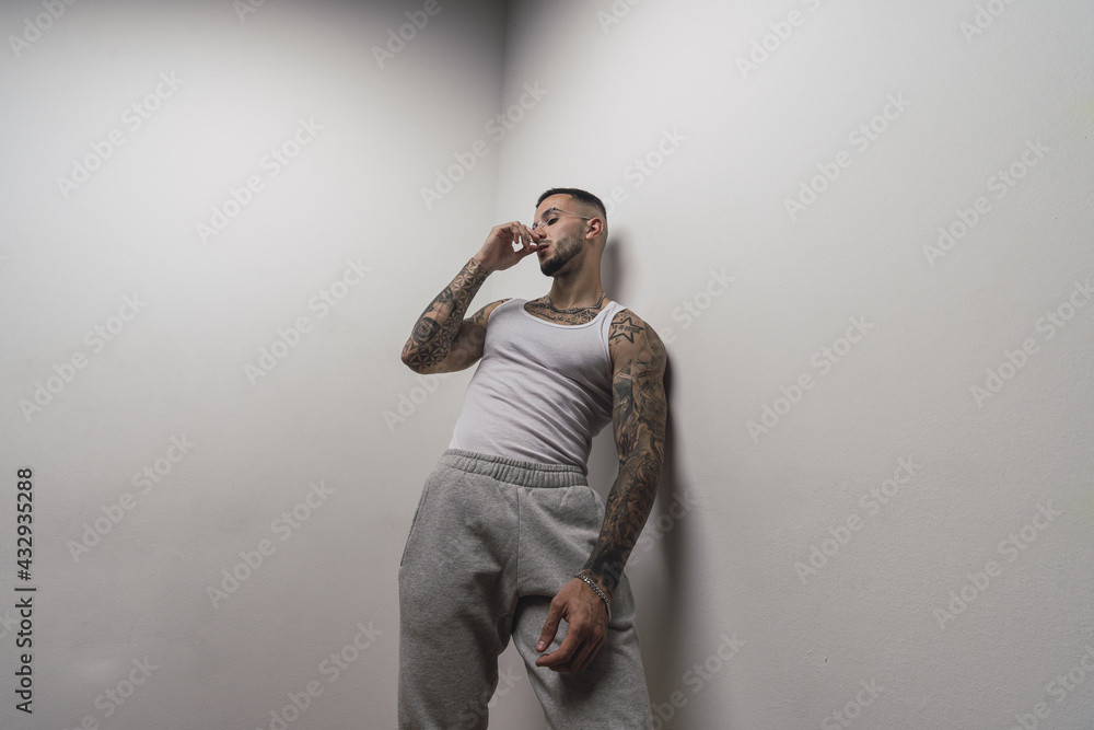 Sticker Portrait of a young handsome tattooed Spanish male posing leaning on a white wall