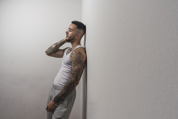 Portrait of a young handsome tattooed Spanish male posing leaning on a white wall
