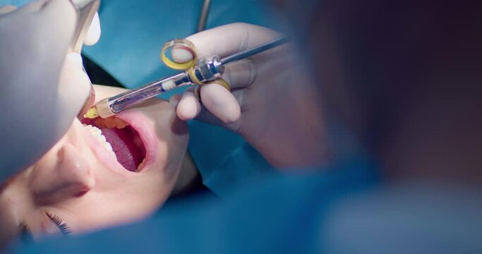 Close-up face of a female patient her mouth are open while a dentist is doing an injection by using the cheek retractor and dental syringe
