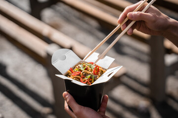 Wok in box in black food container. Holding spicy noodles with chopsticks. Fast food delivery service. Takeaway chinese street meal.
