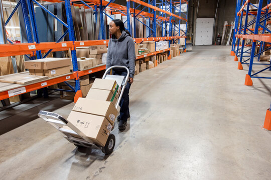 Worker moving boxes with trolley in distribution warehouse