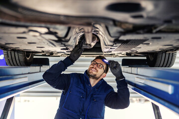 Technical inspection of the car. Car service in the workshop. A man in a blue uniform stands under...
