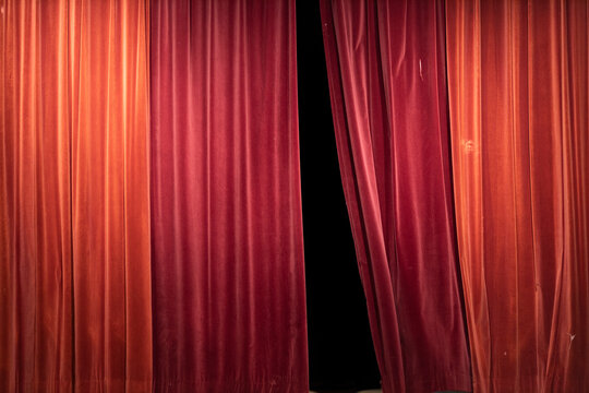 Partly opened washed out discolored vibrant red theatrical curtain with details and texture of the thick cloth hanging straight down. Anticipation and the arts concept.
