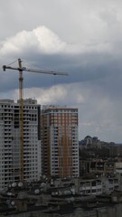 Fototapeta na wymiar Construction site of unfinished multistory building with crane jib at overcast sky background. Under construction cityscape with rooftops and cloudscape. Vertical shot