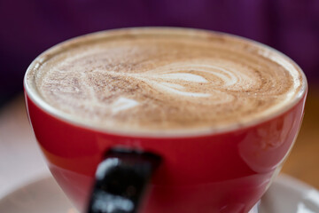 Close-up of freshly made cappuccino coffee in a ceramic red cup. Selective focus. Low depth of field.
