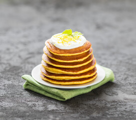 Vegan breakfast lemon pancakes with zest on a plate on a dark gray background