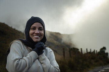 mujer joven  con ropa de invierno parada en una montaña sonriendo - obrazy, fototapety, plakaty