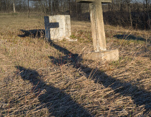 A setting sun casts long shadows of grave markers in the dead grass and onto other headstones.
