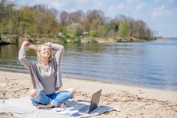 Happy free woman with laptop on the beach by the lake. Freelancer mobile office.