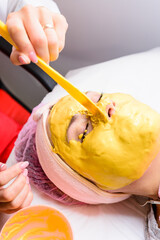 spa treatments in a beauty salon, hand of a professional beautician applying a gold mask on the client's face.