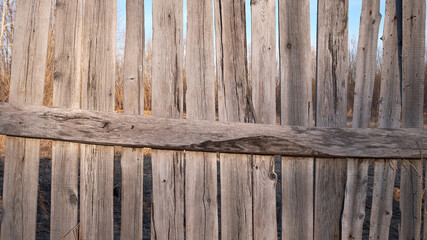 Old wooden fence against sky with clouds. Dilapidated village fence on a cloudy day. Silence and desolation.