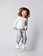 Ginger little girl laughs merrily, jumps and dances in a light T-shirt with a print and an inscription.