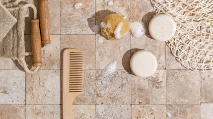 Zero waste bathroom accessories - dry shampoo, exfoliating body strap, natural sea sponge with organic soap foam, wood brush, mesh bag on earth toned stone tales top view direct sunlight