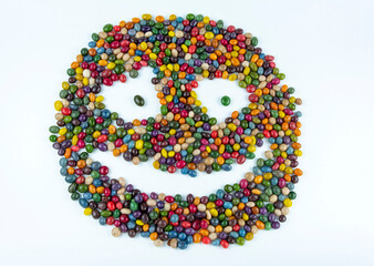 A smiley face made of colorful round candy drops. Assorted bright candy balls or dragees. White background.