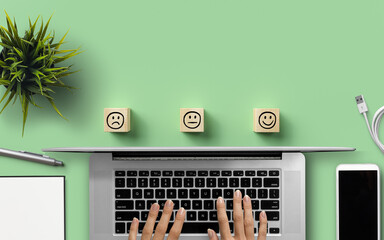 hand typing on a computer surrounded by office tools and wooden cubes with smiley symbols on light...