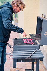 Middle-aged man cooking meat on barbecue grill in backyard of house