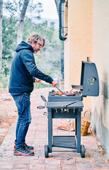 Middle-aged man cooking meat on barbecue grill in backyard of house