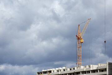 Construction crane on the background of a cloudy sky, construction of a residential complex. Construction of a high-rise building with a crane. Construction concept
