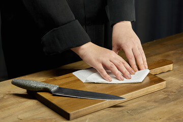 Cleaning of the workplace in the kitchen. Women's hands wipe the cutting board on the kitchen table