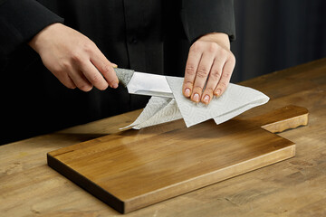 Cleaning of the workplace in the kitchen. Women's hands wipe a kitchen knife