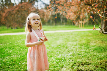 Adorable three year old girl in pink dress enjoying sunny spring day in Park of Sceaux near Paris