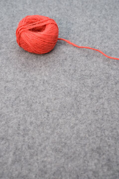 Vertical Shot Of A Red Ball Of Yarn With A Loose String And Copy Text On Gray Background