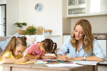 Young beautiful woman mother drawing with colorful pencils with her two cute little kids sisters...