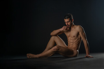 Naklejka premium Fashion nude photo of a male model with seductive figure sitting isolated on the floor in a studio