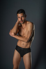 Fototapeta premium Fashion close-up portrait of a handsome male with bare torso posing in black underwear on isolated background
