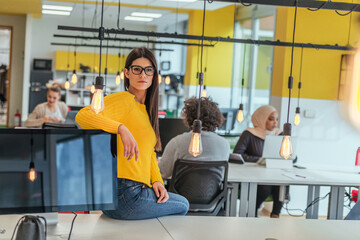 Fototapeta premium Female boss, manager executive posing in a modern startup office while being surrounded by her coworkers, team.