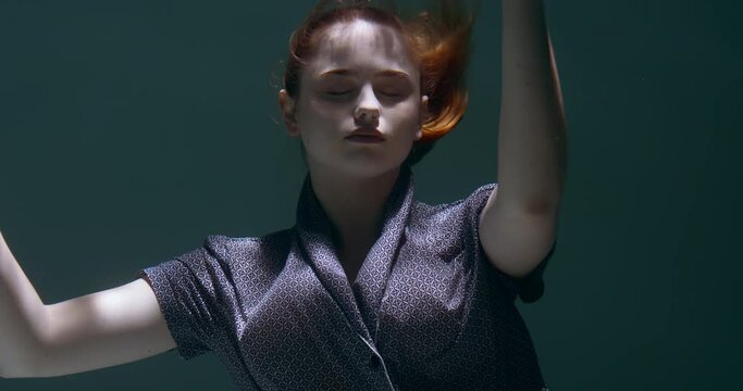 Cinematic portrait of young beautiful woman with eyes closed slowly sinking deep under water falling asleep slow motion.