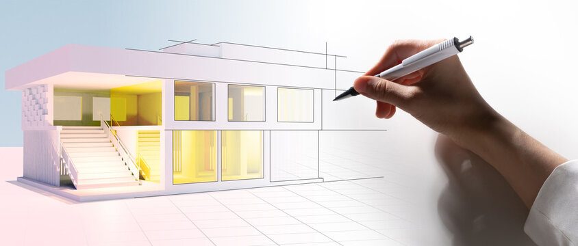 A person draws an image of the future house with a pen. A mock-up of a two-story building with lights in the windows. A human hand with a pen next to a drawing of a building. Designing a new building.