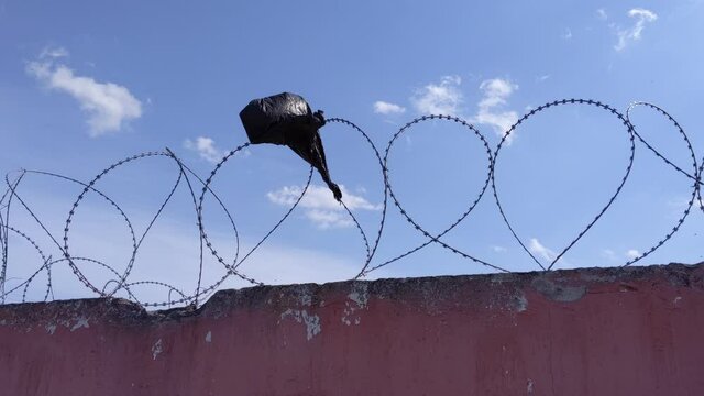 Piece of black plastic bag that has got hooked on the barbed wire fence. 