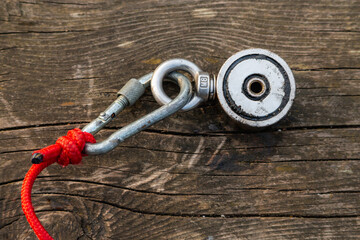 Strong magnet on a red rope carabiner, on a wooden surface. Equipment for magnet fishing