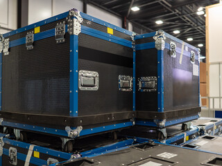 Stackable boxes for the transportation of concert equipment. Black containers with wheels in the exhibition hall. Boxes with wheels, handles and metal corners are mounted on top of each other.