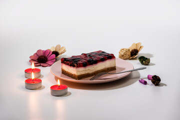 Slice of cheesecake with Raspberry and Currant sauce in a pink plate, with romantic candles set, closeup view. Fruit sauce poured on cheesecake