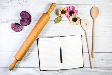 A notebook copy space mockup styled in a kitchen or bakery setting, with a rolling pin and wooden spoons on a wooden surface