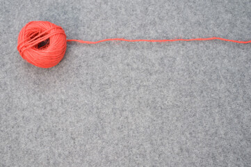 Ball of red yarn with a loose string stretching to the side on a gray background with copy space
