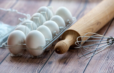 Fresh white eggs with stainless steel whisk and rolling pin on a wooden table. Close uo shot with...