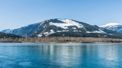 Fototapeta na wymiar early spring Columbia river with snow on mountains blue sky British Columbia Canada