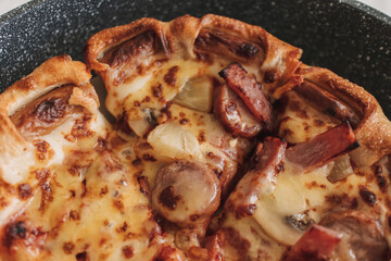 Homemade pizza with sausages and pineapple in a pan.