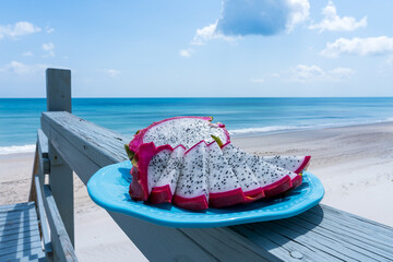 Dragon fruit on a blue plate against a background of blue ocean water. Vacation healthy food concept
