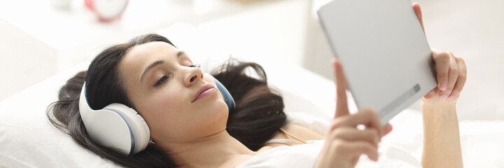Woman with headphones lying on bed and holding tablet