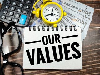 Business concept.Text OUR VALUES with claculator,clock,glasses and banknote on brown wooden background.