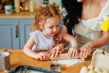 A funny little baby helper is playing with a test on his hands. Baby learns to knead helps adult mom in the kitchen, happy cute little daughter and parent mom have fun making cookies together at home