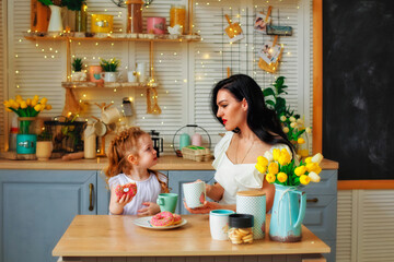 A cheerful family on the background of a bright kitchen. Mom and her daughter girl have fun with colorful donuts.