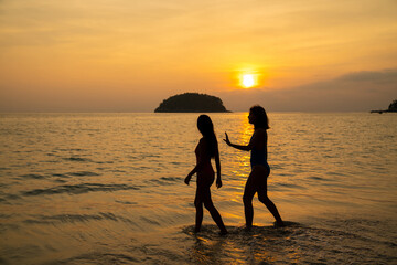Obraz premium Asian woman friendship in colorful swimwear walking and playing sea water together on the beach at summer sunset. Female girl friends enjoy and having fun outdoor activity lifestyle on summer vacation