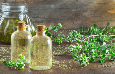 Oregano essential oil bottles and jar over a wooden table surrounded by oregano brenchs with flowers and dried oregano